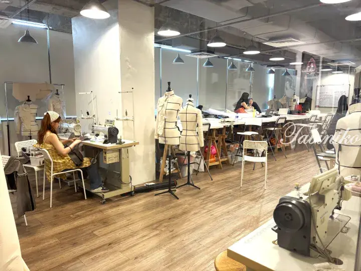 Interior of a fashion design studio with sewing machines, mannequins, and students working on garments.
