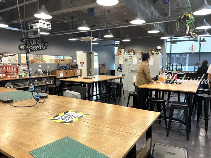 Interior of a modern maker space with wooden work tables, stools, and a Pong Fever sign.