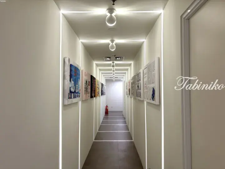 Modern white corridor with LED strip lighting and framed art displays, featuring a red fire extinguisher at the end.