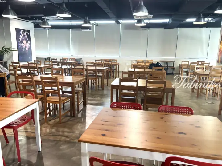 Spacious dining area with wooden tables and chairs, red plastic chairs, and anime wall art in a modern cafe setting.