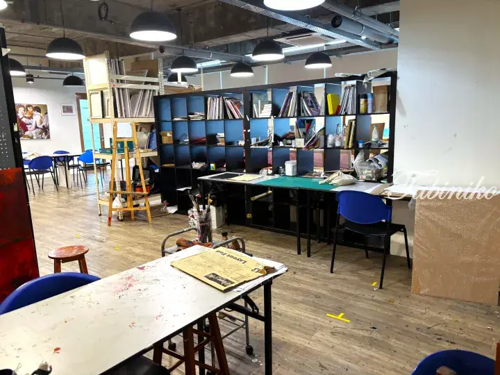 Interior of a creative studio space with wooden floors, work tables, shelves, and art supplies in a modern setting.
