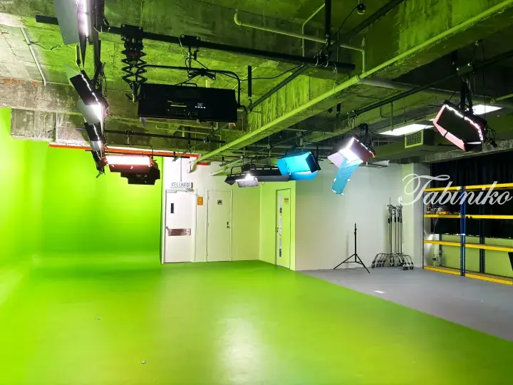 Professional studio setup featuring a green screen, ceiling-mounted lighting rigs, and equipment in a modern space.