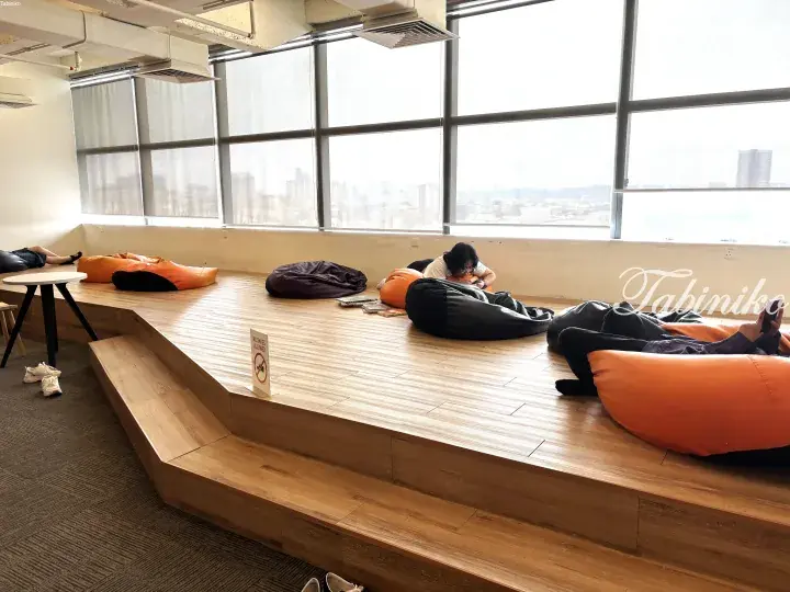 People relaxing on bean bags in a modern co-working space with large windows overlooking a city view.