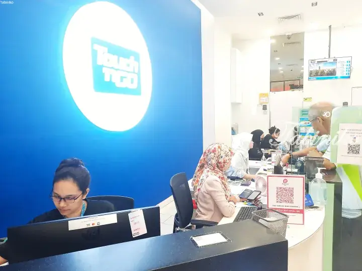 Customers at a Touch &rsquo;n Go counter with staff assisting them in front of a large blue wall with the brand logo.