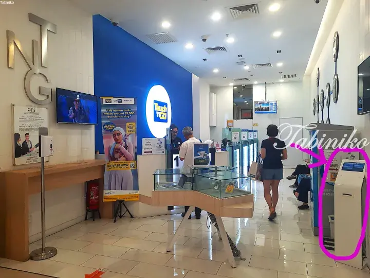 Interior of a Touch &rsquo;n Go store with customers and a self-service kiosk highlighted in pink.