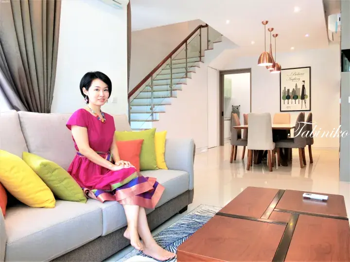 Woman in a pink dress sitting on a sofa in a modern Malaysian home with a staircase and dining area.