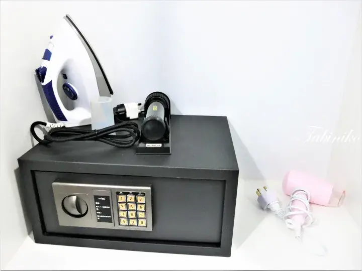 A black digital safe with an iron and flashlight on top, next to a pink hairdryer.