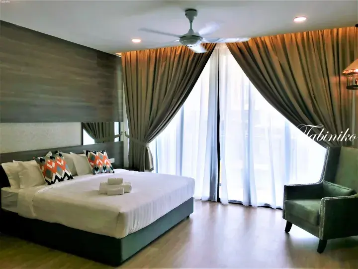 Modern hotel room with a large bed, decorative pillows, and floor-to-ceiling curtains.