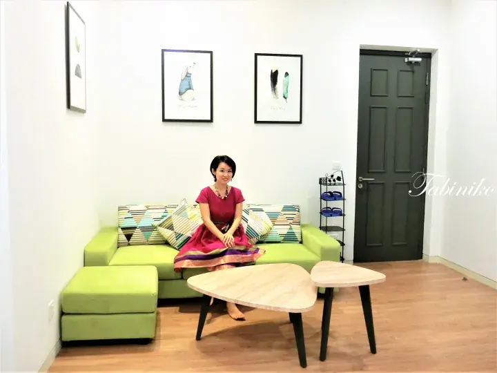 Woman in a pink dress sitting on a green sofa in a modern apartment living room with wooden coffee tables.