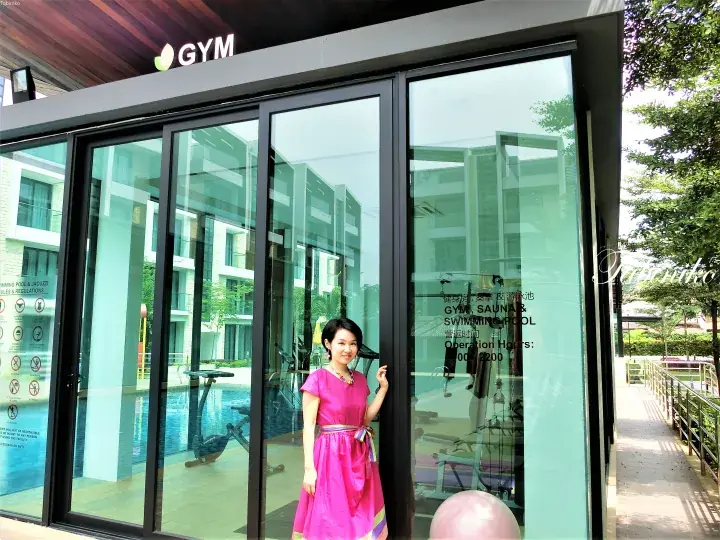 Woman in pink dress standing at the glass entrance of a modern gym and swimming pool facility.