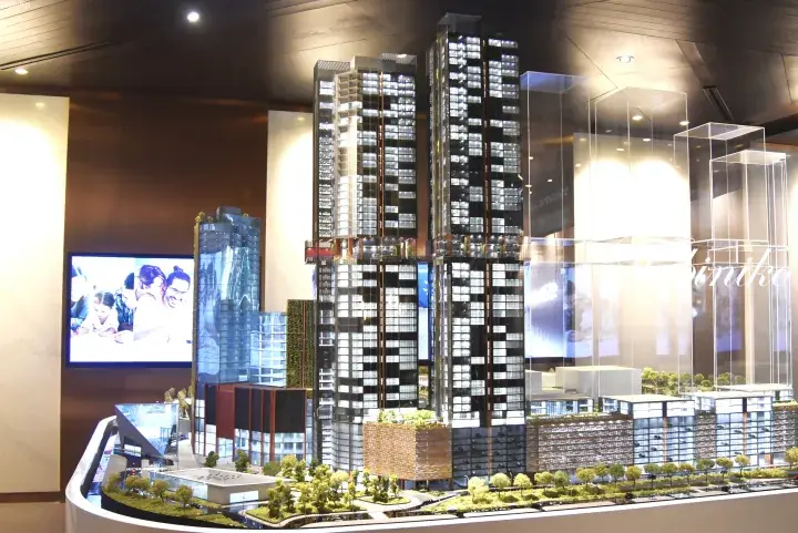 Architectural model of a modern high-rise residential development with glass towers, greenery, and a display screen.