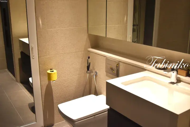 Modern bathroom with beige tiles, wall-mounted toilet, bidet, and white rectangular sink.