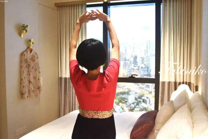 Woman stretching on a bed in a high-rise hotel room with a city view.