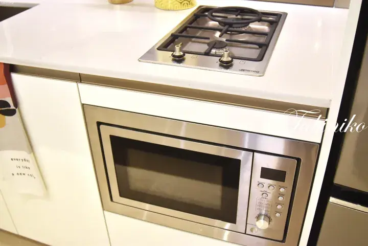 Modern kitchen featuring a built-in stainless steel microwave oven and a gas cooktop on a white countertop.