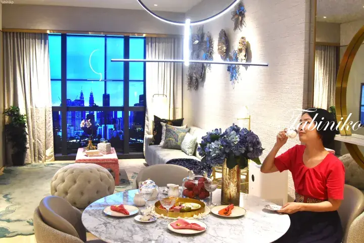 Woman enjoying afternoon tea at a marble table with a view of the Petronas Twin Towers from a luxury Kuala Lumpur hotel suite.