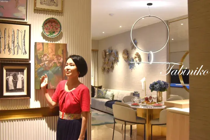 Woman in red top admiring art in a luxury property showroom with modern dining area and elegant decor.