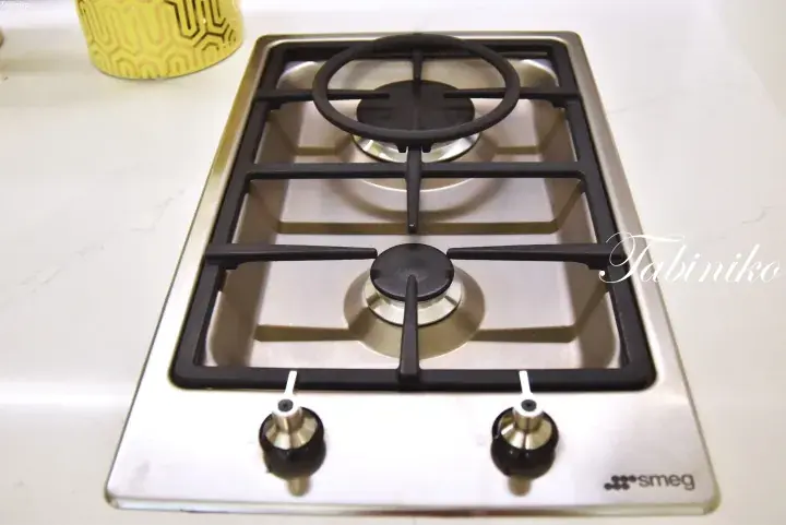 Close-up of a stainless steel Smeg two-burner gas hob with black grates and control knobs on a white countertop