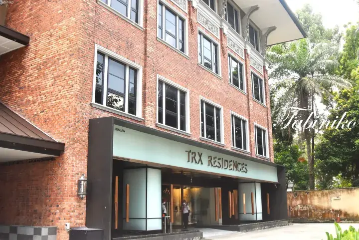 TRX Residences entrance featuring a red brick facade, modern glass doors, and lush tropical greenery.