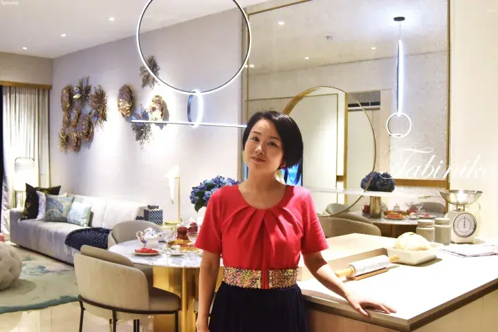 Woman in red top standing in a modern luxury showroom kitchen with marble dining table and designer lighting.