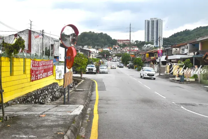 Street view in Malaysia showing a yellow wall, convex mirror, and a tall residential tower in the background.
