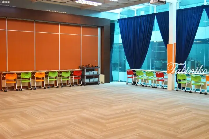 Bright classroom with colorful chairs, orange wall panels, and blue curtains in a modern Malaysian property.