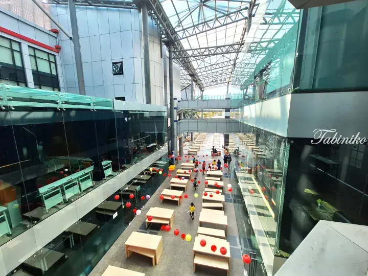Spacious atrium with glass walls and skylight, featuring wooden tables and colorful lanterns for a festive atmosphere.