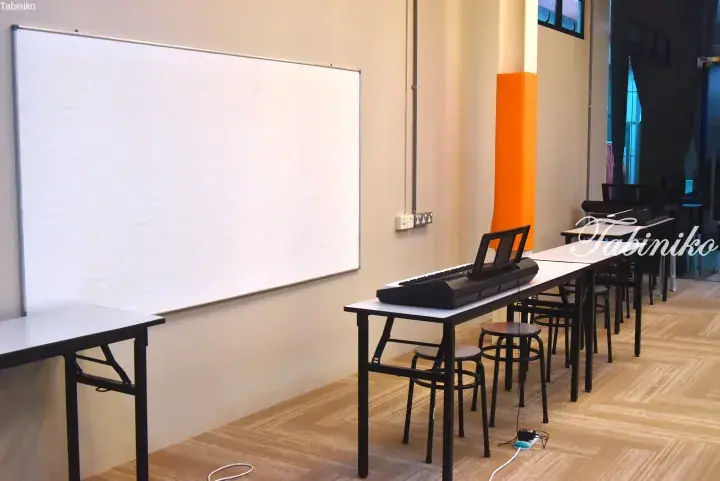 Music lesson room with digital keyboards on tables and a large whiteboard in a bright space.