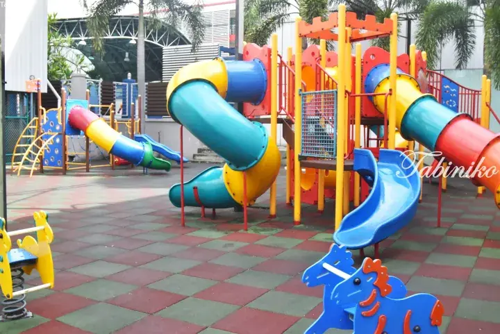Colorful playground with slides and spring riders on rubber flooring at a Malaysia residential property.