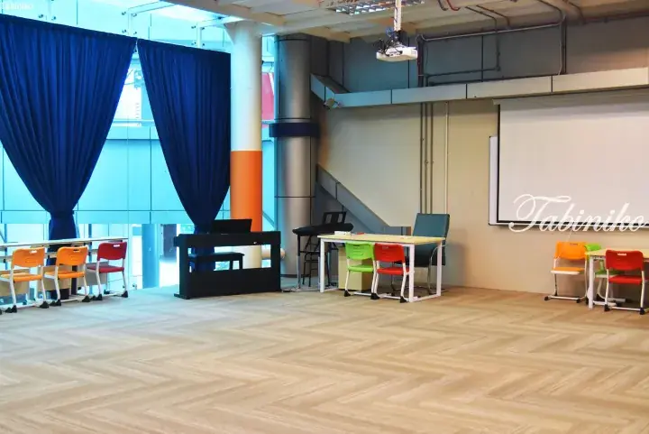 Bright classroom with colorful chairs, digital pianos, and blue curtains in a modern space.