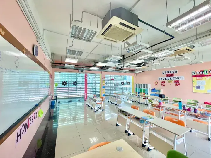 Bright classroom with pink walls, student desks, and motivational signs like ‘Strive for Excellence’ and ‘Honesty’.