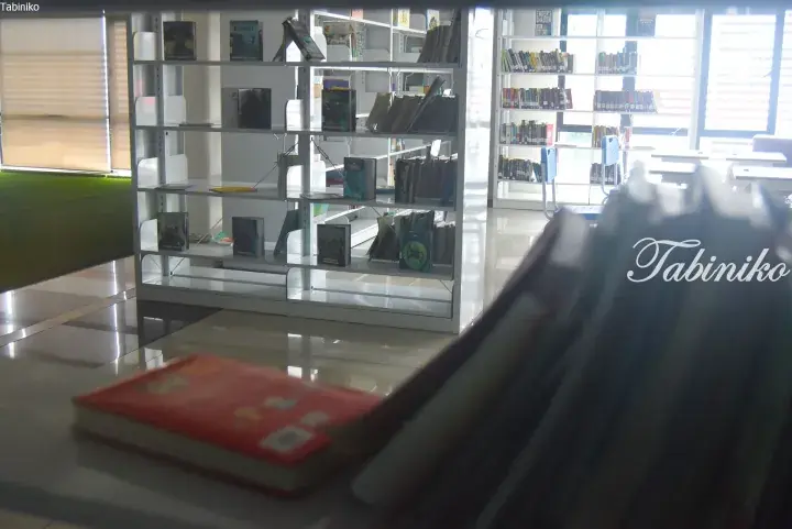 Modern library interior with white bookshelves filled with books and a red book on a table in the foreground.