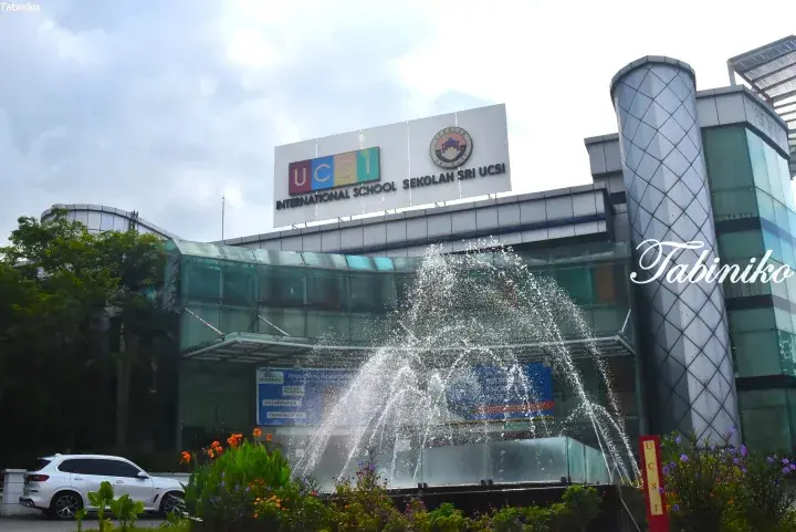 Modern glass facade of UCSI International School with a prominent sign and a water fountain in the foreground.
