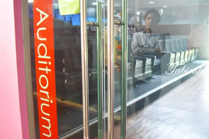 Glass door with red vertical sign reading Auditorium, revealing a man inside a room with rows of seating.