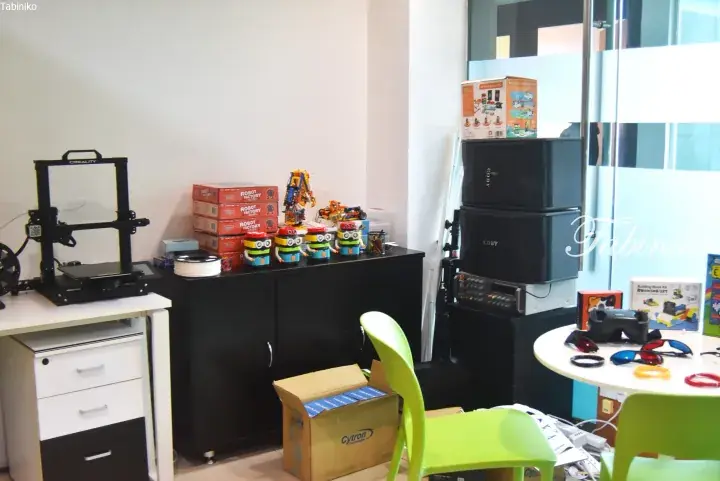 A classroom with a 3D printer, robot kits, and VR equipment on tables and shelves.