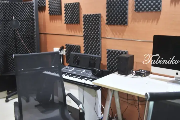 Home studio setup with a keyboard, computer, and acoustic foam panels on wooden walls.