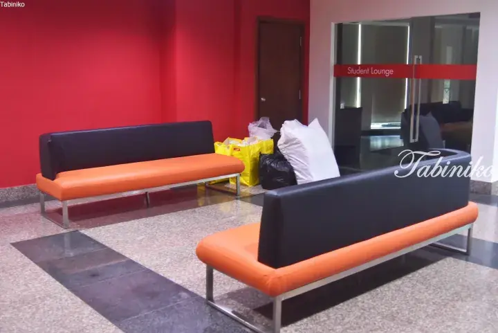 Orange and black sofas in a modern student lounge area with red walls and glass doors.