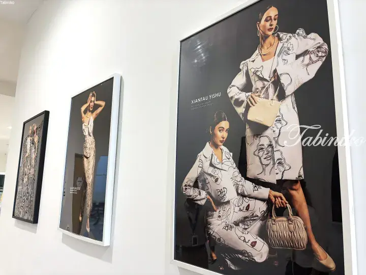Framed fashion design posters displayed on a white gallery wall featuring models in elegant outfits.