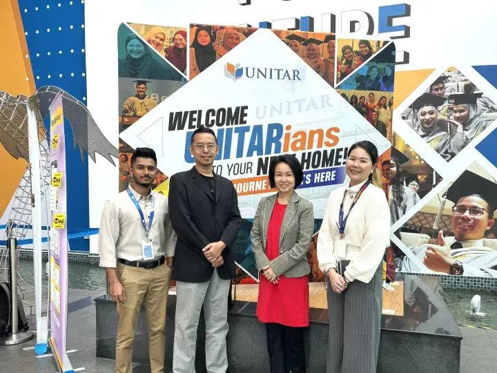 Four people pose in front of a UNITAR welcome banner at an event.