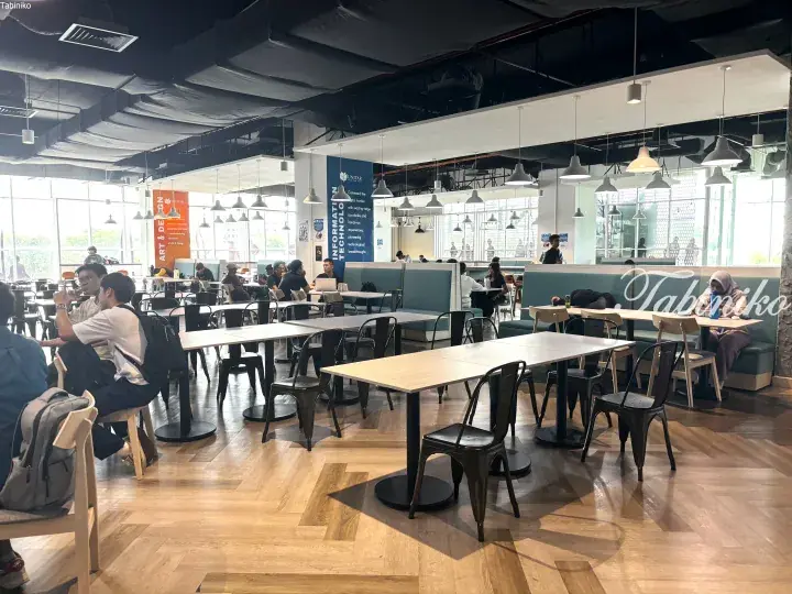Modern campus study area with wooden floors, tables, and students studying under pendant lights.