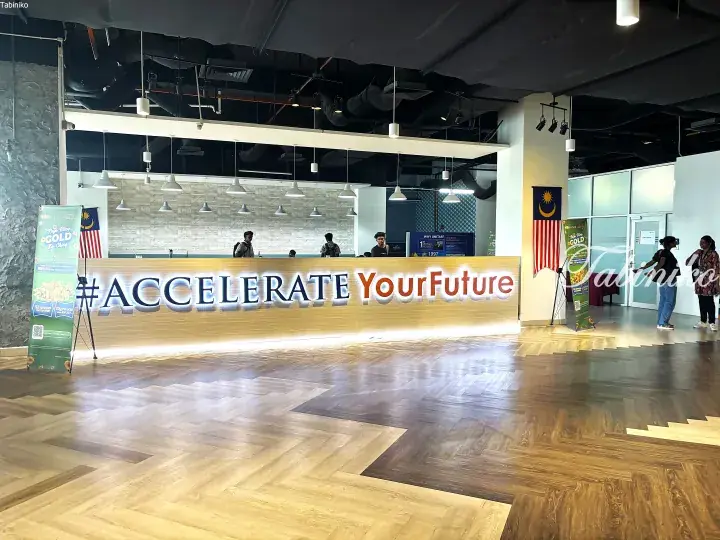 Modern UNITAR university reception area with a large illuminated #AccelerateYourFuture sign and Malaysian flags.