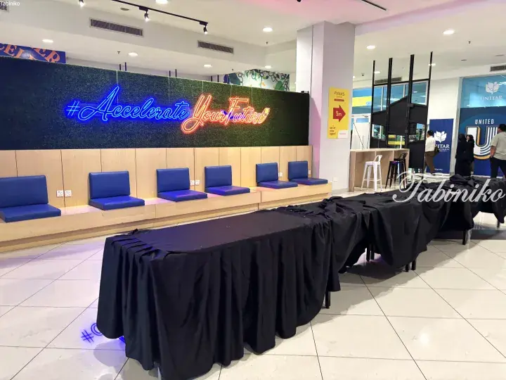 Neon sign reading Accelerate Your Future above blue seating at UNITAR booth in Malaysian mall.
