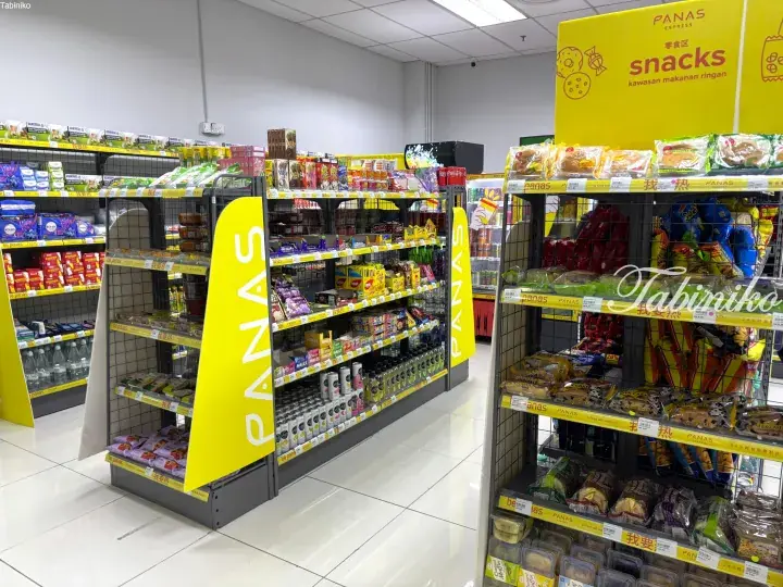 Bright interior of a PANAS Express convenience store showing snack aisles stocked with chips, cakes, and drinks.