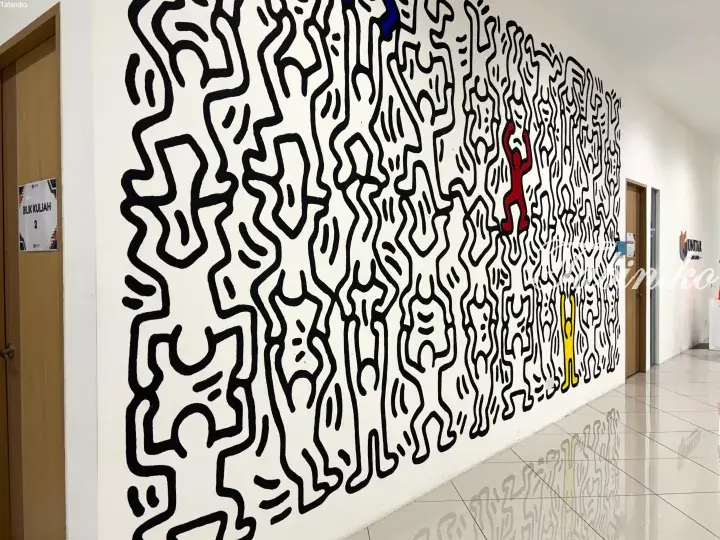 Keith Haring-style mural with black line figures on a white wall in a UNITAR College hallway.