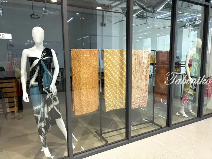 Mannequins displaying batik fashion designs in a glass-fronted studio window.