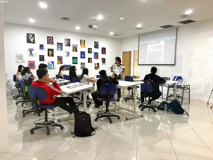 Instructor teaching art students in a bright classroom with colorful student artwork displayed on the walls.