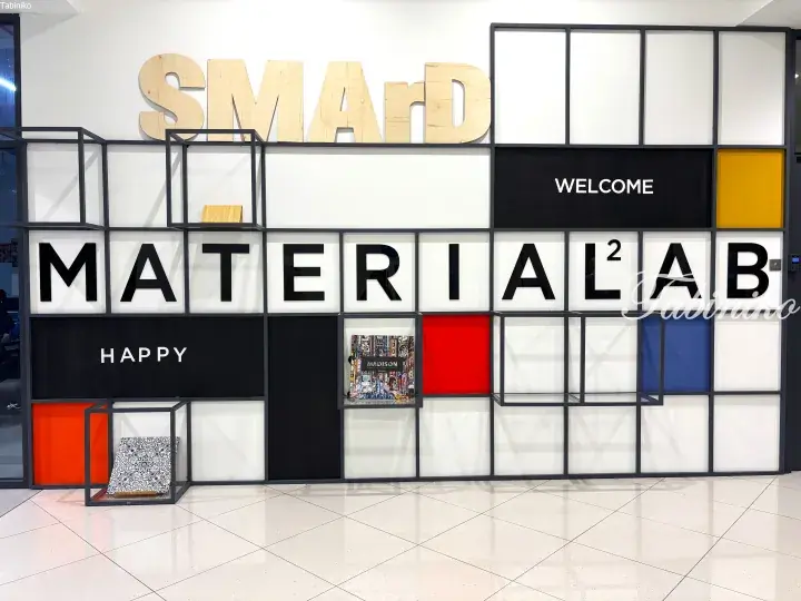 Modern interior wall display featuring large wooden ‘SMART’ letters and ‘MATERIAL²’ text in a grid design with colorful panels.
