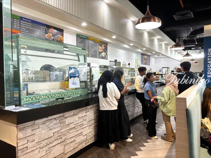 Students queue at a modern cafeteria counter with menu boards displaying Western and Asian food options.