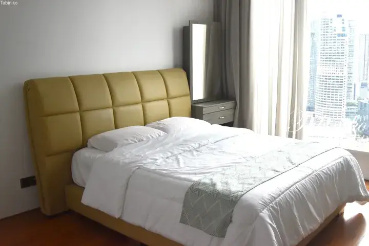 Yellow leather bed with white linens in a modern high-rise apartment overlooking Kuala Lumpur city skyline