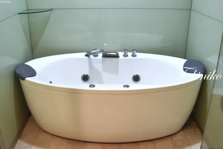 White oval jacuzzi bathtub with chrome fixtures and headrests in a modern bathroom with glass walls