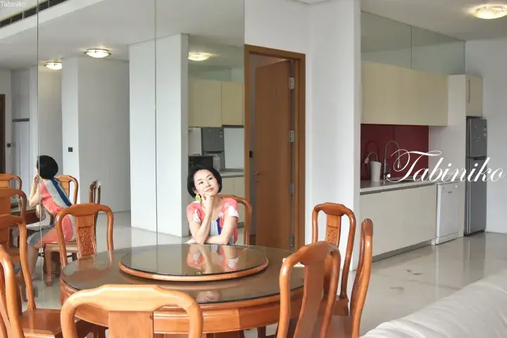 Woman sitting at a round wooden dining table with a lazy susan in a modern apartment with mirrored walls and a kitchen.